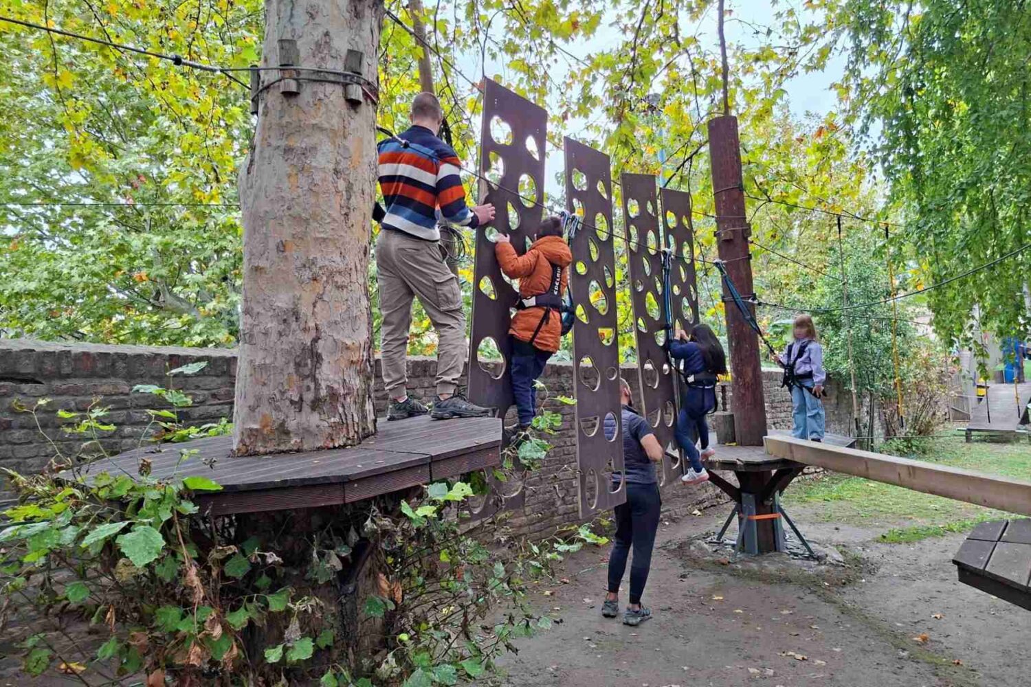 Deca se igraju i penju na strukturi u Dečjem Zoo vrtu, okružena zelenilom i životinjama.