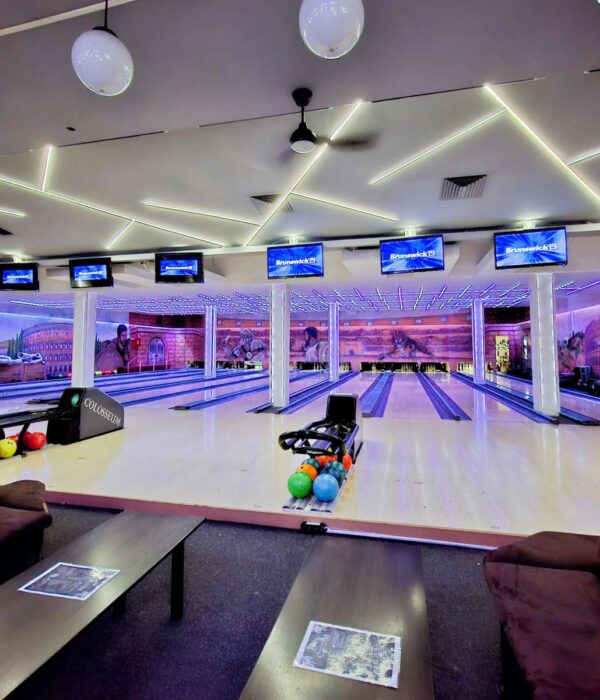Panoramski pogled na enterijer Colosseum Bowling centra, obuhvata više staza za kuglanje, stolove za sedenje i monitori za rezultate.