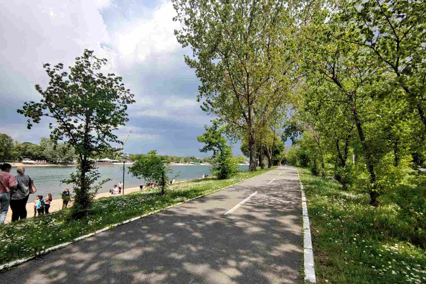 Biciklistička staza na Adi Ciganliji, okružena zelenilom, pored jezera sa bistrom vodom.